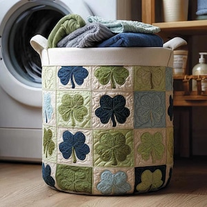 Può includere: Un cesto per la biancheria rotondo con un motivo a trifoglio trapuntato nei toni del verde e del blu. Il cesto è pieno di asciugamani piegati e ha due manici. Lo sfondo comprende una lavatrice e mensole in legno.
