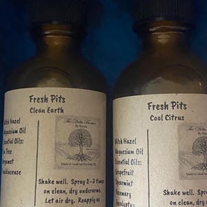 Könnte beinhalten: Zwei braune Glassprühflaschen mit der Aufschrift Fresh Pits, eine in Clean Earth und eine in Cool Citrus. Jedes Etikett listet Inhaltsstoffe wie Hamamelis, Magnesiumöl und ätherische Öle auf, zusammen mit Anweisungen zum Schütteln und Auftragen.