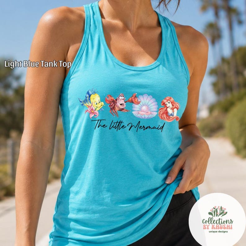 May include: A light blue racerback tank top featuring a graphic print of characters from The Little Mermaid, including a yellow fish, a red crab, a pink seashell with a pearl, and a mermaid, with the text The Little Mermaid printed below.