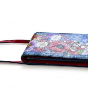 May include: A red and floral crossbody bag with a long strap. The bag features a colorful floral design on the front flap, with red accents and a matching strap. The bag is designed to be worn over the shoulder.
