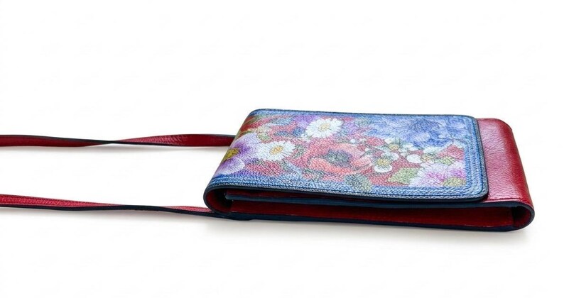 May include: A red and floral crossbody bag with a long strap. The bag features a colorful floral design on the front flap, with red accents and a matching strap. The bag is designed to be worn over the shoulder.