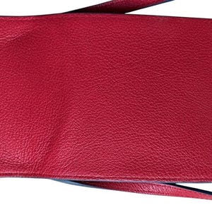 May include: A red leather crossbody bag with a textured surface. The bag has a long strap and a snap closure. The interior is also red. The bag is designed to hold a phone and other small items.