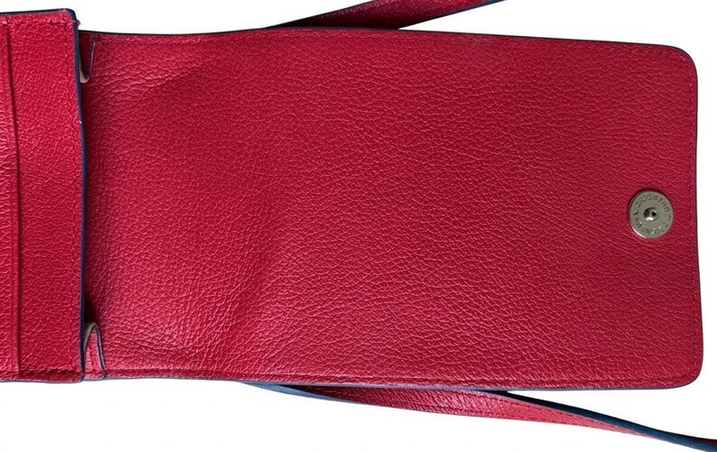 May include: A red leather crossbody bag with a textured surface. The bag has a long strap and a snap closure. The interior is also red. The bag is designed to hold a phone and other small items.