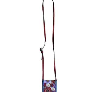 May include: A rectangular crossbody bag with a floral design. The bag features a red leather base and strap, with a colorful floral print on the front. The strap is long and adjustable. The flowers are in shades of red, purple, blue, and white.