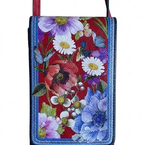 May include: Red crossbody bag with a floral design. The bag features a vibrant print of various flowers in shades of purple, white, and blue against a red background. The bag has a blue border and a red strap.