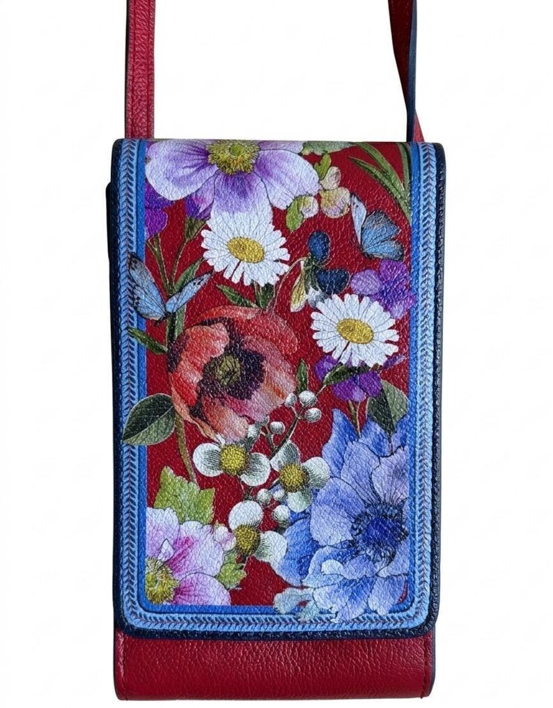May include: Red crossbody bag with a floral design. The bag features a vibrant print of various flowers in shades of purple, white, and blue against a red background. The bag has a blue border and a red strap.