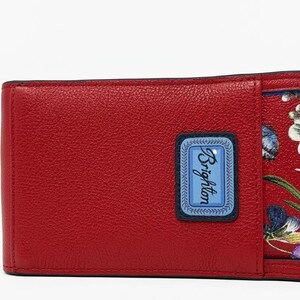 May include: A red leather wallet with a floral design. The wallet has a rectangular shape with a blue label that says "Brighton". The interior features a red floral pattern with white, purple, and green flowers.
