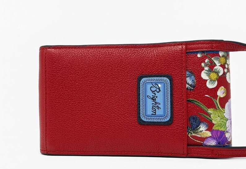 May include: A red leather wallet with a floral design. The wallet has a rectangular shape with a blue label that says "Brighton". The interior features a red floral pattern with white, purple, and green flowers.