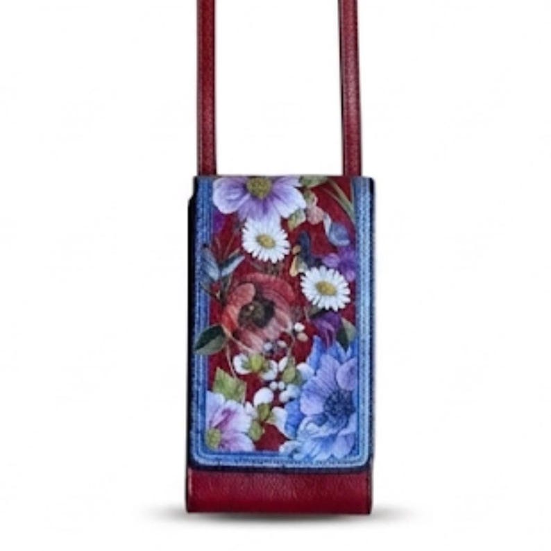 May include: A burgundy leather crossbody bag with a floral print. The bag features a rectangular shape with a flap closure and a long, thin strap. The floral design includes red, purple, and blue flowers against a red background.