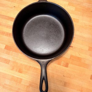 May include: A black cast iron frying pan with a long handle and a hanging loop. The pan is round with a flat cooking surface and a raised edge. The number "8" is stamped on the handle.