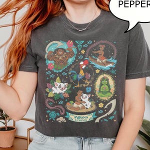 May include: Dark gray t-shirt featuring a colorful graphic of characters from the animated film Moana. The design includes images of Maui, Moana, Hei Hei, Pua, and other characters. The word "Pepper" is in a speech bubble.