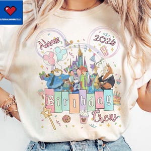 May include: Cream-colored t-shirt featuring a colorful graphic of Disney's Zootopia characters. The design includes the text "Name" and "2020" within Mickey Mouse ear outlines, and the words "Birthday Crew". The design also includes a castle, balloons, and a birthday cake.
