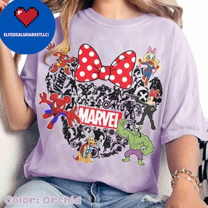May include: Orchid-colored t-shirt featuring a red polka-dot bow and various Marvel characters. The word "MARVEL" is displayed in a red and white rectangular box. The shirt includes images of Spider-Man, Hulk, and Iron Man.