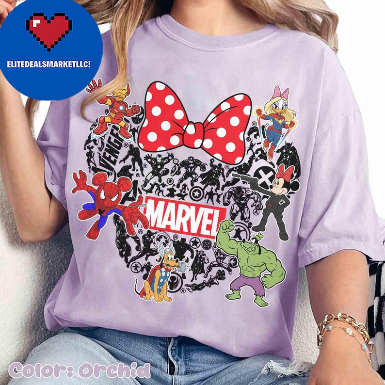 May include: Orchid-colored t-shirt featuring a red polka-dot bow and various Marvel characters. The word "MARVEL" is displayed in a red and white rectangular box. The shirt includes images of Spider-Man, Hulk, and Iron Man.