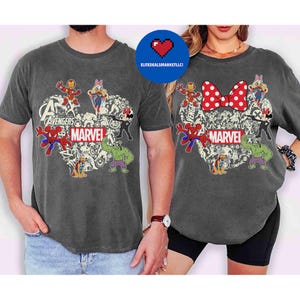 May include: Two charcoal gray t-shirts featuring a heart-shaped design with Marvel characters. The design includes Spider-Man, Hulk, Iron Man, and Mickey and Minnie Mouse. The word "MARVEL" is printed in white.