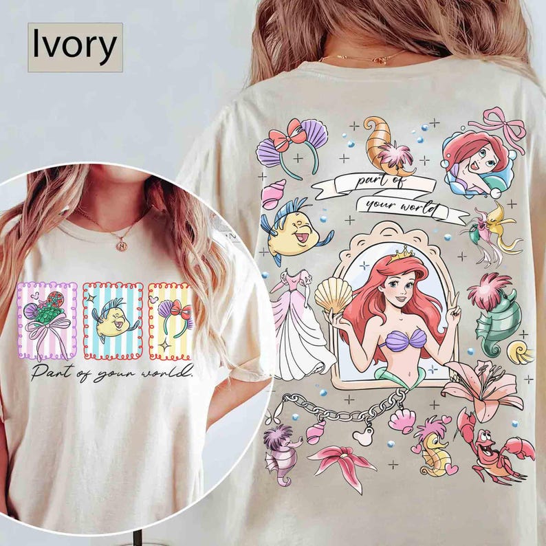 May include: Ivory-colored t-shirt featuring a colorful graphic design. The front displays three framed illustrations with the text "Part of your world." The back showcases a larger design with Ariel and other characters.