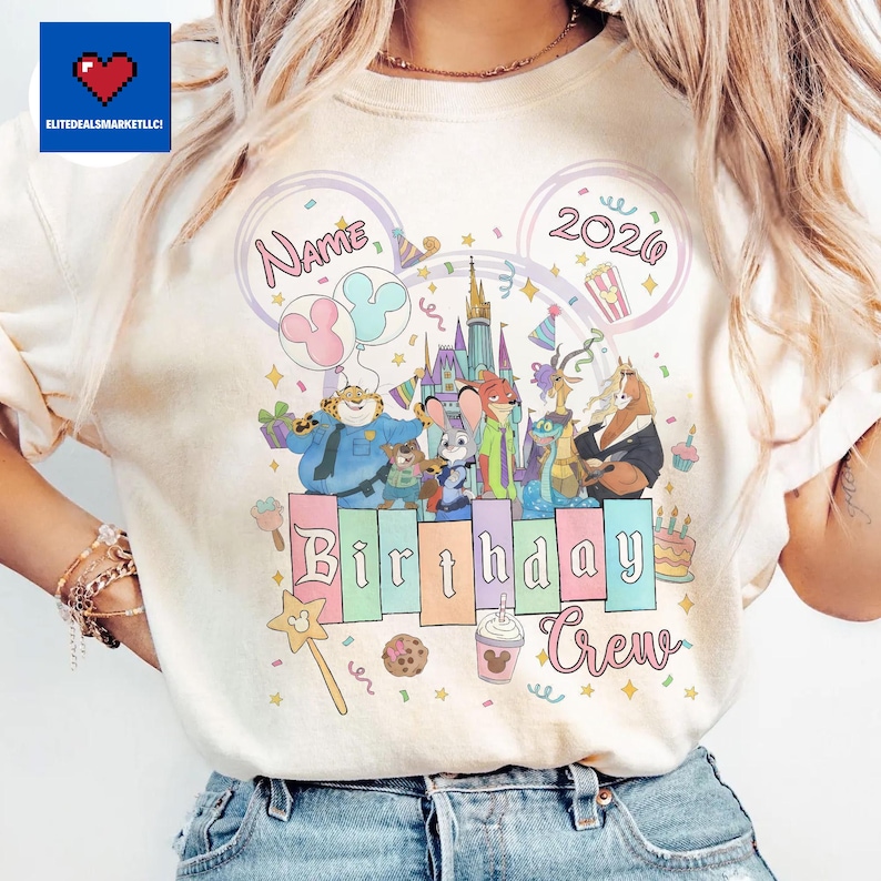 May include: Cream-colored t-shirt featuring a colorful graphic of Disney's Zootopia characters. The design includes the text "Name" and "2020" within Mickey Mouse ear outlines, and the words "Birthday Crew". The design also includes a castle, balloons, and a birthday cake.