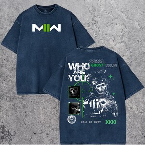 May include: Dark blue t-shirt with the text "MW" in white and green on the front. The back features a graphic of a skull soldier with the text "WHO ARE YOU?" and "SIMON GHOST RILEY" in white and green. The shirt also has the text "CALL OF DUTY".
