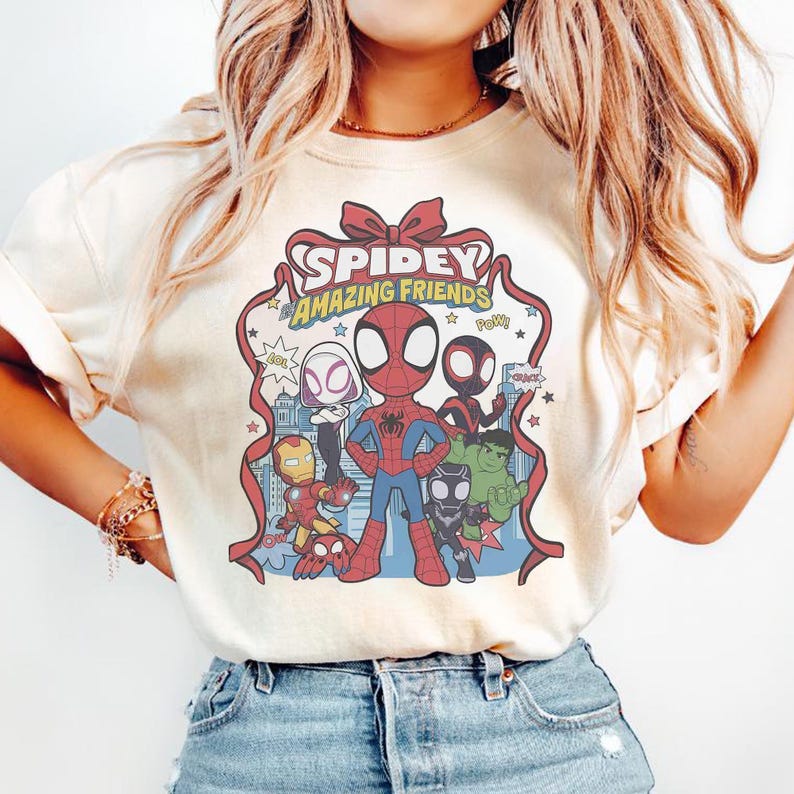 May include: Cream-colored t-shirt featuring a cartoon graphic of Spidey and his Amazing Friends. The design includes Spider-Man, Iron Man, Hulk, and other characters, with the text "Spidey Amazing Friends" in a red ribbon design.