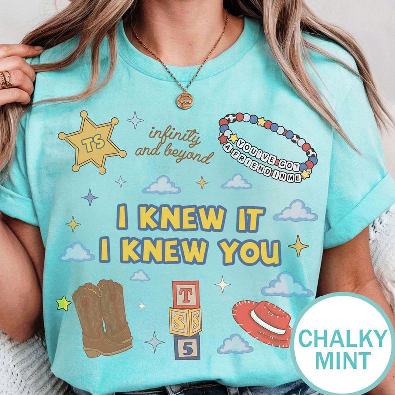 May include: A light mint green t-shirt featuring a graphic print with a yellow sheriff star, a beaded bracelet with text, brown cowboy boots, alphabet blocks, a red hat, and the phrases infinity and beyond and I KNEW IT I KNEW YOU with clouds.