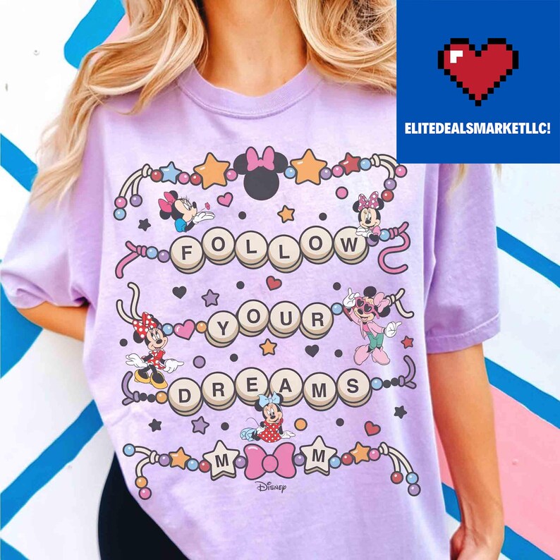 May include: A light purple t-shirt featuring a colorful graphic design with the text "FOLLOW YOUR DREAMS". The design includes images of Minnie Mouse and stars, with the Disney logo at the bottom.