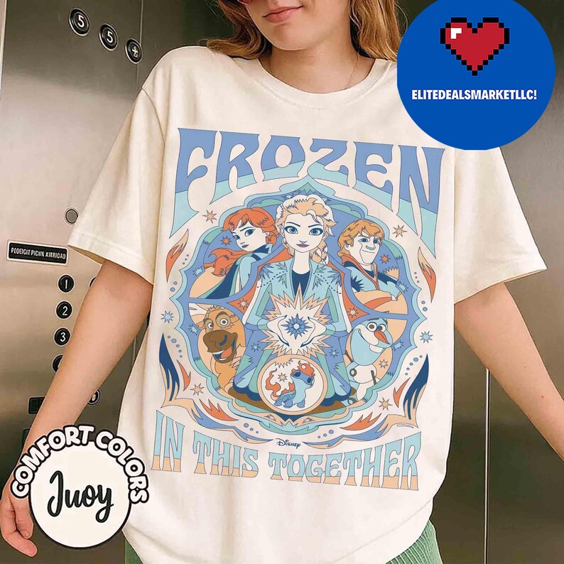 K&ouml;nnte beinhalten: Cremefarbenes T-Shirt mit einer Grafik aus dem Disney-Film Frozen. Das Design enth&auml;lt die W&ouml;rter "FROZEN" und "IN THIS TOGETHER" mit Bildern der Charaktere. Das Shirt ist von der Marke Comfort Colors.