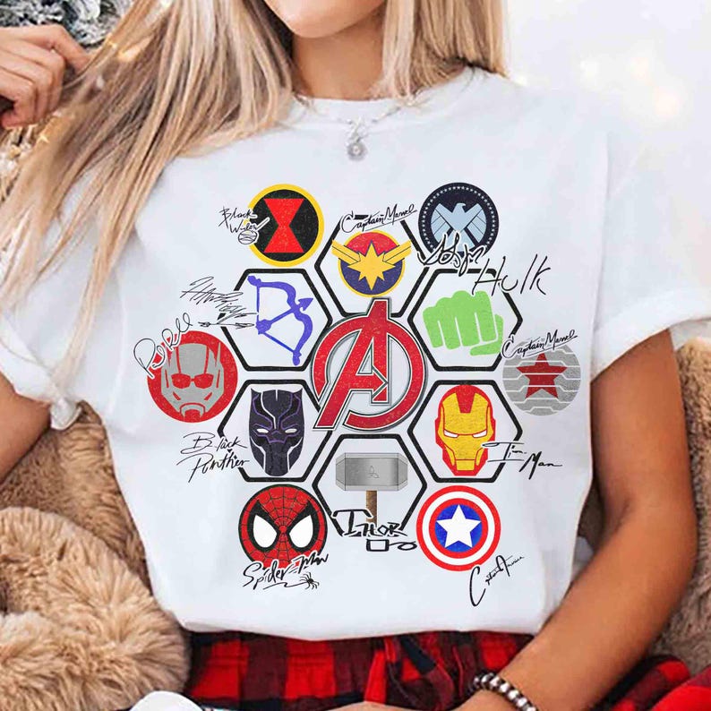 Pu&ograve; includere: T-shirt bianco con una grafica colorata raffigurante vari loghi e firme di supereroi, tra cui Iron Man, Captain Marvel e Spider-Man. Il logo degli Avengers &egrave; ben visibile al centro. La maglietta ha maniche corte.