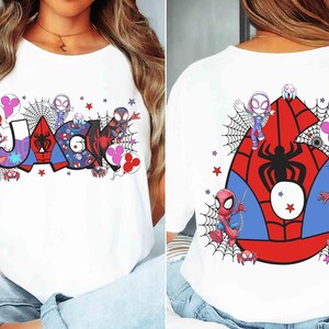 Puede incluir: Camiseta blanca con un dise&ntilde;o gr&aacute;fico colorido. La parte delantera muestra el nombre "JACK" en estilo c&oacute;mic, rodeado de telara&ntilde;as, estrellas y personajes de dibujos animados. La parte trasera presenta un gran n&uacute;mero seis con un dise&ntilde;o de ara&ntilde;a.