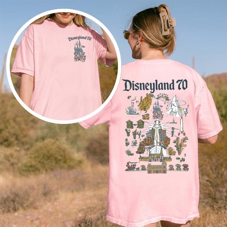 Puede incluir: Una camiseta de manga corta de color rosa claro con un peque&ntilde;o logotipo de Disneyland 70 en el pecho y un gr&aacute;fico grande y detallado en la espalda que muestra varias atracciones del parque, monumentos y el texto Disneyland 70 en oscuro.