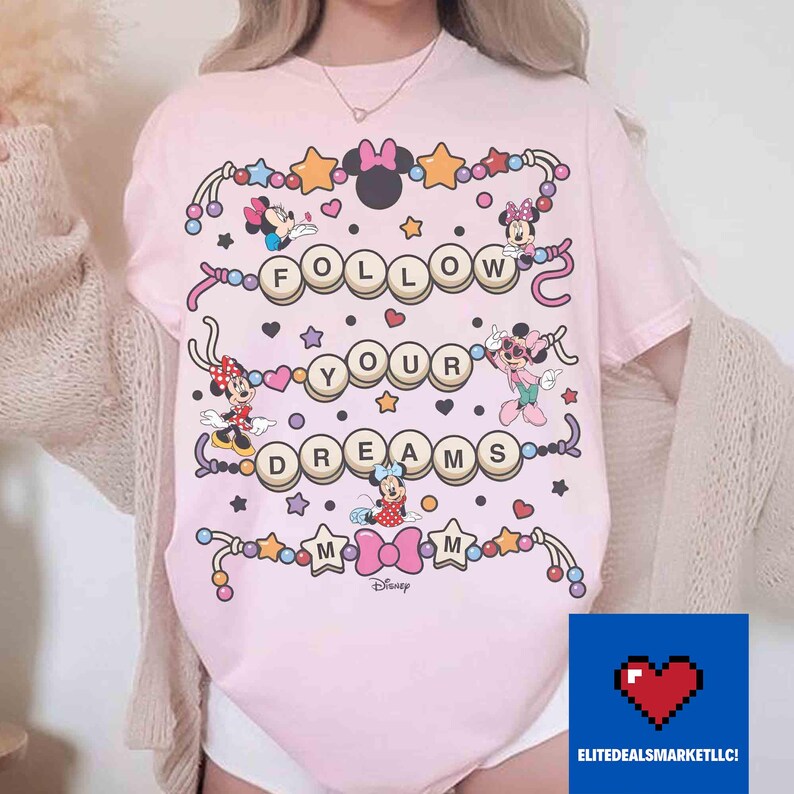 May include: Pink t-shirt featuring Minnie Mouse characters and the phrase "FOLLOW YOUR DREAMS" in a playful design. The shirt includes stars, hearts, and decorative elements, with the Disney logo at the bottom.