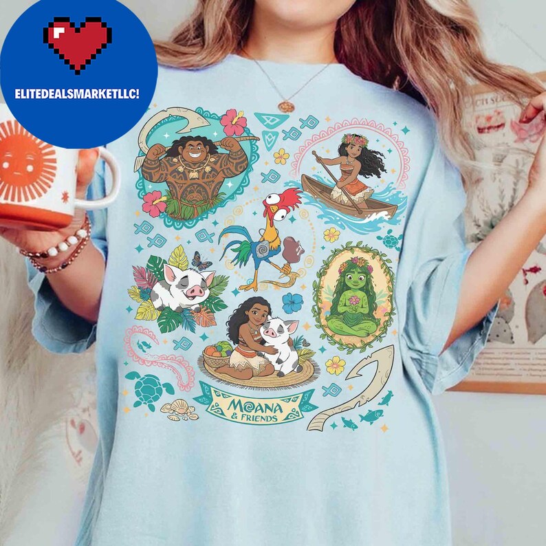 May include: Light blue t-shirt featuring colorful cartoon illustrations of characters from the movie Moana. The shirt includes images of Maui, Moana, Pua, Hei Hei, and other elements from the film. The text "Moana & Friends" is also visible.