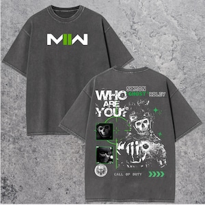 May include: Dark gray t-shirt with the text "MW" in white and green on the front. The back of the shirt features a graphic of a skull-faced soldier with the text "WHO ARE YOU?" and "SIMON GHOST RILEY". The shirt also has the text "CALL OF DUTY".