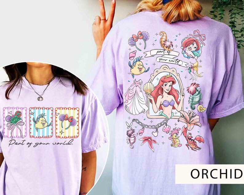 May include: Orchid-colored t-shirt featuring a colorful graphic of Ariel from The Little Mermaid, with the text "Part of your world." The design includes various characters and elements from the movie. The shirt is a comfortable, casual style.