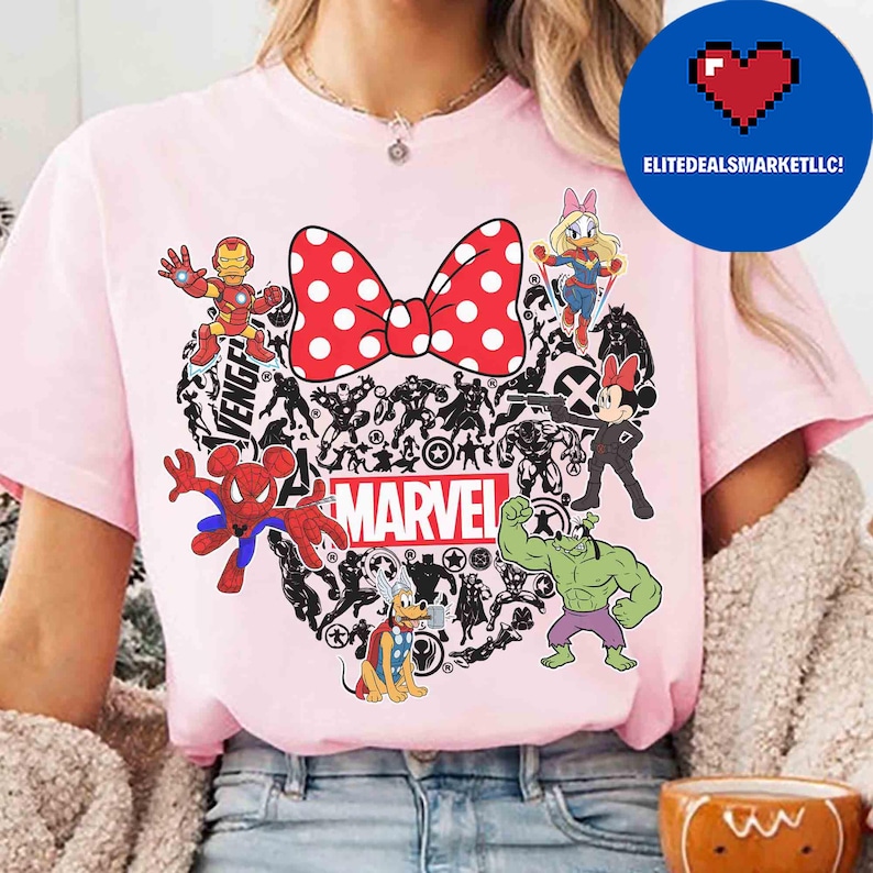 May include: Pink t-shirt featuring a heart-shaped design with Marvel characters and a red polka-dot bow. The shirt includes Iron Man, Spider-Man, Hulk, and Minnie Mouse. The word "MARVEL" is printed in white.