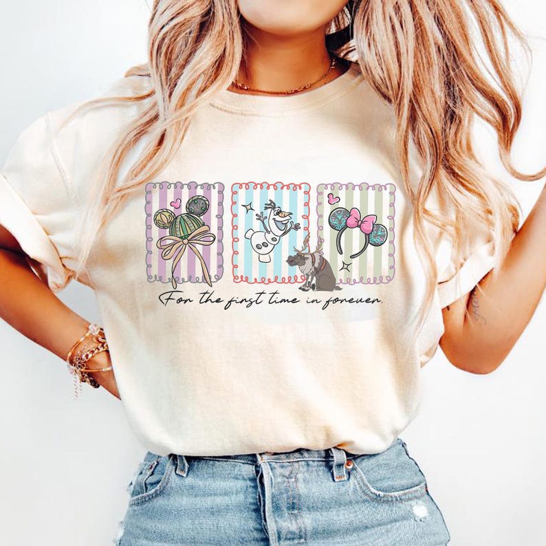May include: Cream-colored t-shirt featuring three framed illustrations with Disney-themed designs. The illustrations include Mickey Mouse ears, Olaf the snowman, and Minnie Mouse ears. The text "For the first time in forever" is printed below the illustrations.