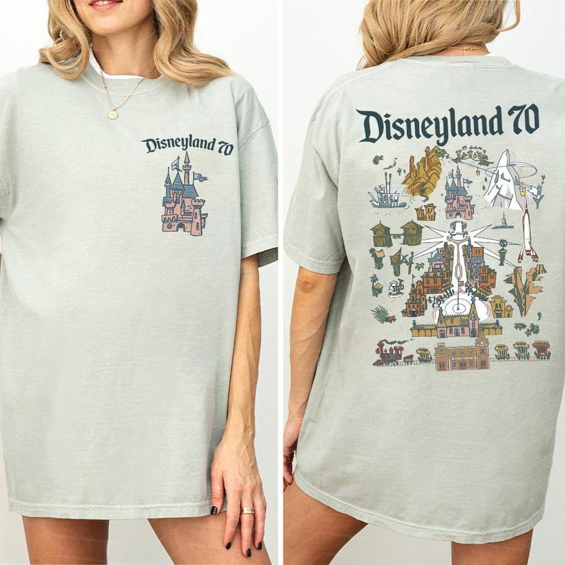 Puede incluir: Una camiseta de color verde salvia claro con un peque&ntilde;o logotipo de Disneyland 70 y un gr&aacute;fico de castillo en el pecho izquierdo. La parte posterior muestra una ilustraci&oacute;n grande y detallada de las atracciones de Disneyland con el texto Disneyland 70.