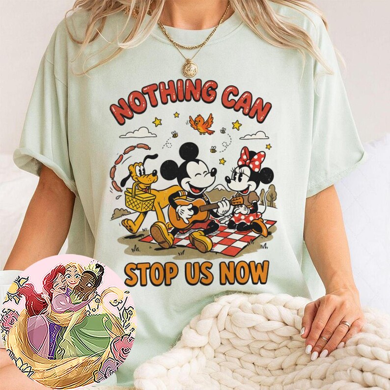 May include: A light green t-shirt featuring a graphic of Mickey Mouse playing a guitar, Minnie Mouse, and Pluto on a picnic blanket. The text reads NOTHING CAN STOP US NOW. A circular inset shows an illustration of three animated characters hugging.