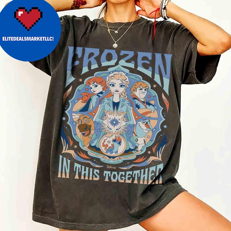 K&ouml;nnte beinhalten: Dunkelgraues T-Shirt mit einer farbenfrohen Grafik aus dem Disney-Film Frozen. Das Design enth&auml;lt die W&ouml;rter "FROZEN" und "IN THIS TOGETHER" mit Bildern von Elsa, Anna, Kristoff, Olaf und Sven. Das T-Shirt hat einen Rundhalsausschnitt.