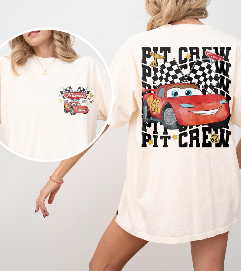 May include: An off-white t-shirt featuring a red race car graphic on the front left chest and a large back print. The back design displays a red race car, checkered flags, and the text PIT CREW with a Route 66 sign. The front graphic includes the word Name.
