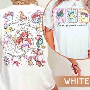 May include: White t-shirt featuring a colorful graphic of Ariel from The Little Mermaid. The design includes Ariel, Flounder, and other sea-themed elements. The text "part of your world" is also included in the design.