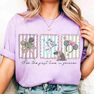 May include: A lilac-colored t-shirt featuring three framed illustrations with Disney-themed designs. The shirt includes images of Mickey Mouse ears, Olaf the snowman, and reindeer. The text "For the first time in forever" is printed below the illustrations.