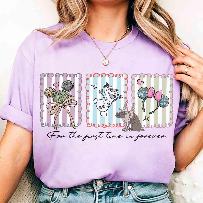 May include: A lilac-colored t-shirt featuring three framed illustrations with Disney-themed designs. The shirt includes images of Mickey Mouse ears, Olaf the snowman, and reindeer. The text "For the first time in forever" is printed below the illustrations.