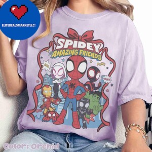 May include: Orchid-colored t-shirt featuring a graphic of Spidey and his Amazing Friends. The design includes Spider-Man, Spider-Gwen, Miles Morales, Iron Man, Hulk, and other characters. The text "Spidey and Amazing Friends" is displayed in a ribbon design.