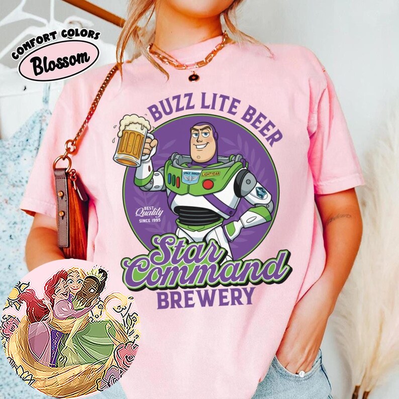 Może przedstawiać: Jasnor&oacute;żowy t-shirt z grafiką przedstawiającą strażnika kosmosu trzymającego kufel piwa wewnątrz fioletowego koła. Napis głosi BUZZ LITE BEER STAR COMMAND BREWERY. Okrągła wstawka przedstawia trzy animowane postacie z długimi włosami, kt&oacute;re się przytulają.