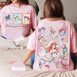 May include: Pink t-shirt featuring a front graphic with three framed images and the text "Part of your world." The back graphic showcases Ariel and other characters from The Little Mermaid. The shirt is a light pink color.