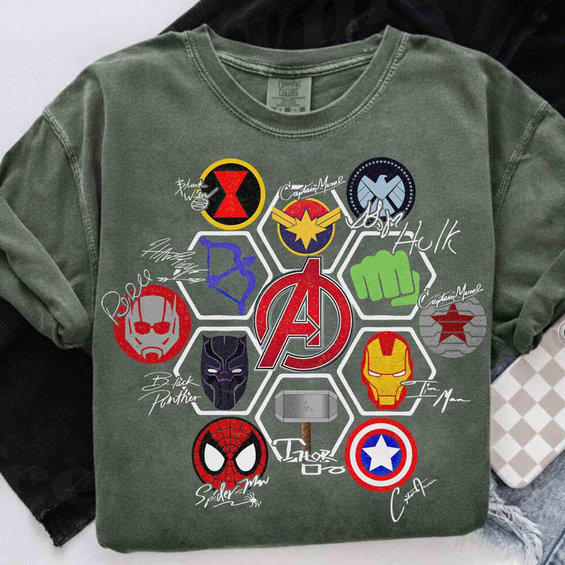 Pu&ograve; includere: Felpa girocollo verde con vari loghi e firme di supereroi. I loghi includono Black Widow, Captain Marvel, Hulk, Iron Man, Black Panther, Spider-Man e Captain America. Il logo degli Avengers &egrave; ben visibile.