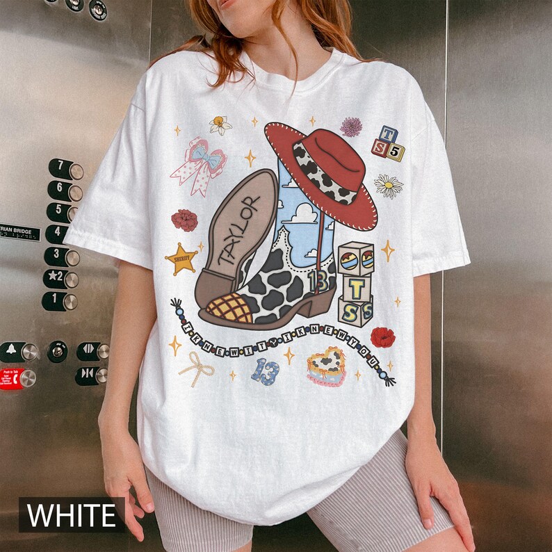 Puede incluir: Una camiseta blanca con un estampado gr&aacute;fico de una bota vaquera con patr&oacute;n de vaca, un sombrero vaquero rojo, un cielo azul, bloques de alfabeto, un lazo y el texto "TAYLOR" y "13". El dise&ntilde;o incluye peque&ntilde;os detalles de flores y estrellas.