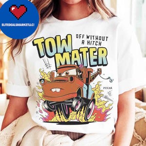 May include: White t-shirt with a cartoon image of Tow Mater from the Pixar Cars film. The design includes the text "TOW MATER" in large, colourful letters, with the phrase "OFF WITHOUT A HITCH" above. The Pixar logo is also visible.