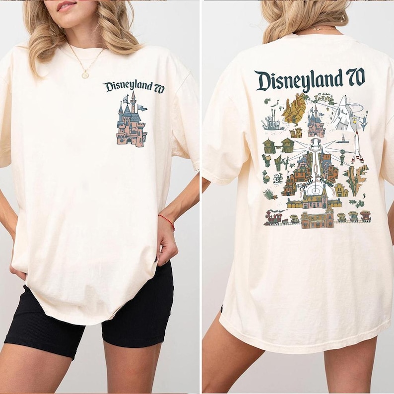Puede incluir: Una camiseta color crema con un peque&ntilde;o gr&aacute;fico de un castillo y el texto Disneyland 70 en el pecho izquierdo. La parte posterior muestra una ilustraci&oacute;n grande y detallada de un mapa de atracciones de Disneyland con el texto Disneyland 70.