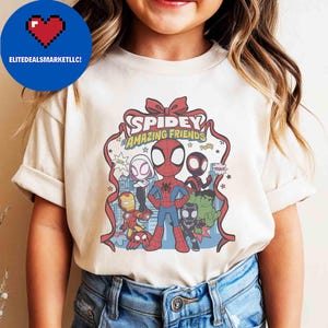 May include: A cream-colored t-shirt featuring a Spidey and His Amazing Friends graphic. The design includes Spiderman, Iron Man, Hulk, and other characters. The text "Spidey Amazing Friends" is displayed in a red ribbon design.